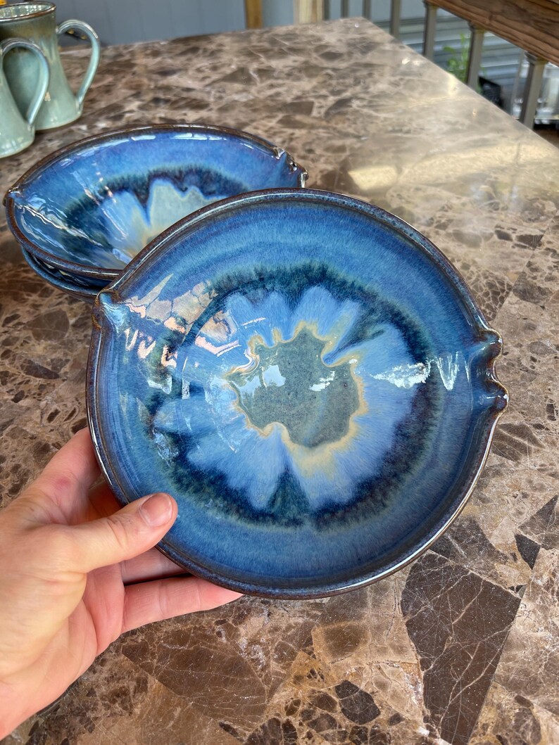 Puede incluir: Cuencos de cer&aacute;mica hechos a mano con un vibrante esmalte azul. Los cuencos tienen un dise&ntilde;o &uacute;nico con un borde azul oscuro y un interior azul claro y crema. Cada cuenco tiene dos peque&ntilde;as asas en los lados. Perfectos para servir sopas, ensaladas u otros platos.