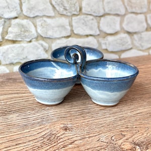 May include: A ceramic serving dish featuring three interconnected bowls with a glossy finish. The bowls display a gradient of deep blue at the rims transitioning to a lighter, pale blue at the base. A central looped handle connects the three bowls.