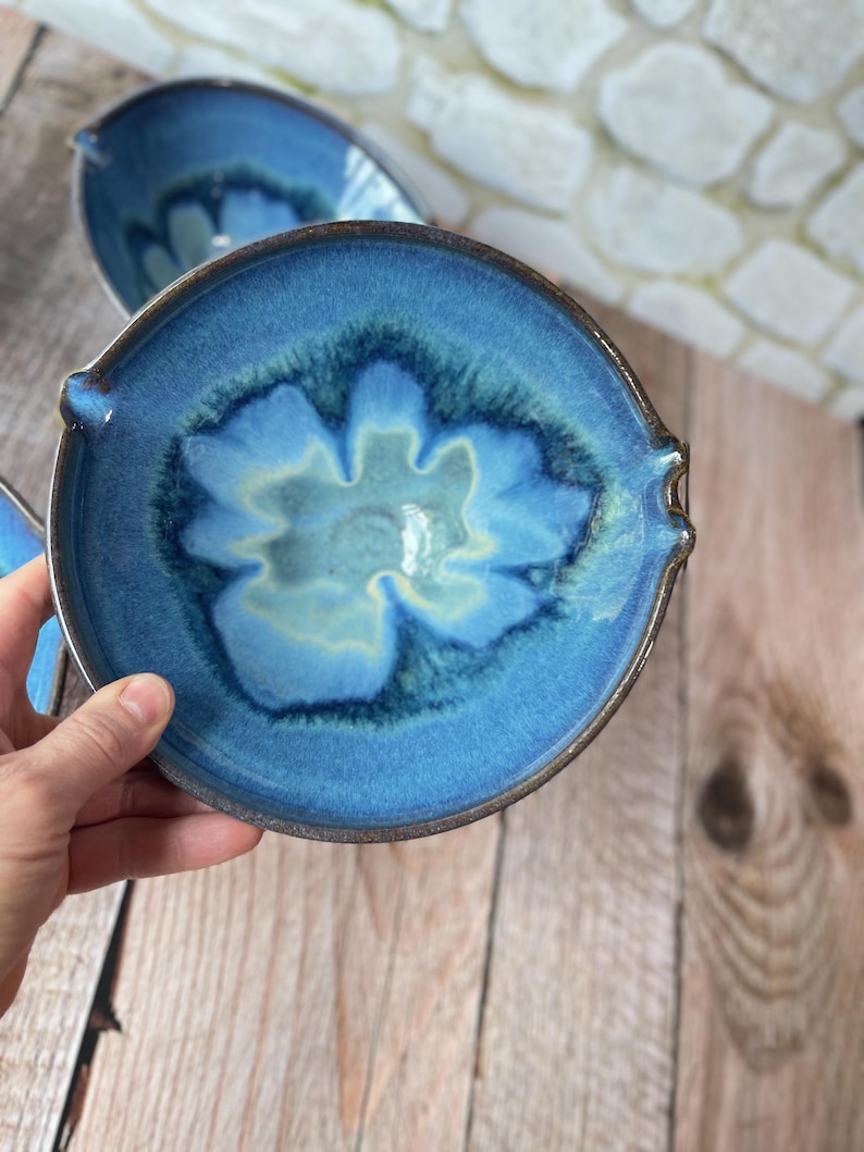 Puede incluir: Un juego de tres cuencos de cer&aacute;mica hechos a mano con un esmalte azul brillante. Cada cuenco presenta un dise&ntilde;o floral &uacute;nico en el centro, con una paleta de colores azul claro y crema. Los cuencos tienen peque&ntilde;as asas a cada lado.