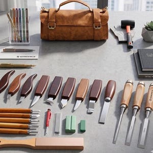 May include: A comprehensive woodworking tool set featuring a brown leather tool roll, various carving knives with wooden handles, three chisels with 11mm and 16mm markings, a mallet, a sharpening stone, a pencil, and a clear acrylic pen holder.