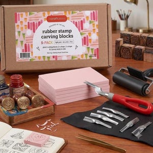 May include: A rubber stamp carving kit featuring a cardboard box labeled incraftables, five light pink 6 inch by 4 inch by 1 inch rubber blocks, a black brayer roller, a red-handled carving tool with six interchangeable metal blades, and tweezers.