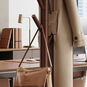 May include: A wooden coat rack with a beige fedora hat, a tan overcoat, and a brown leather messenger bag. The rack has multiple pegs for hanging items. The scene is set in an office environment.