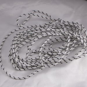 May include: White rope with a repeating pattern of small black dashes. The rope is coiled and appears to be made of a durable material, suitable for various uses. The rope is against a white background.