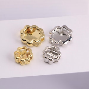 Puede incluir: Cuatro cuentas met&aacute;licas en forma de flor, doradas y plateadas. Dos son doradas y dos son plateadas. Las cuentas tienen un borde festoneado y un centro hueco. Las cuentas son probablemente para la fabricaci&oacute;n de joyas u otras manualidades.