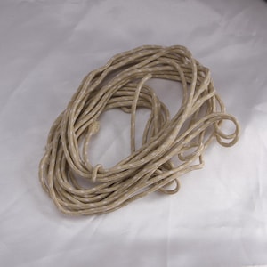 May include: A coiled rope with a tan and white speckled pattern. The rope is tightly wound, with visible strands and a knot. The neutral color palette suggests versatility for various uses, from crafting to outdoor activities.