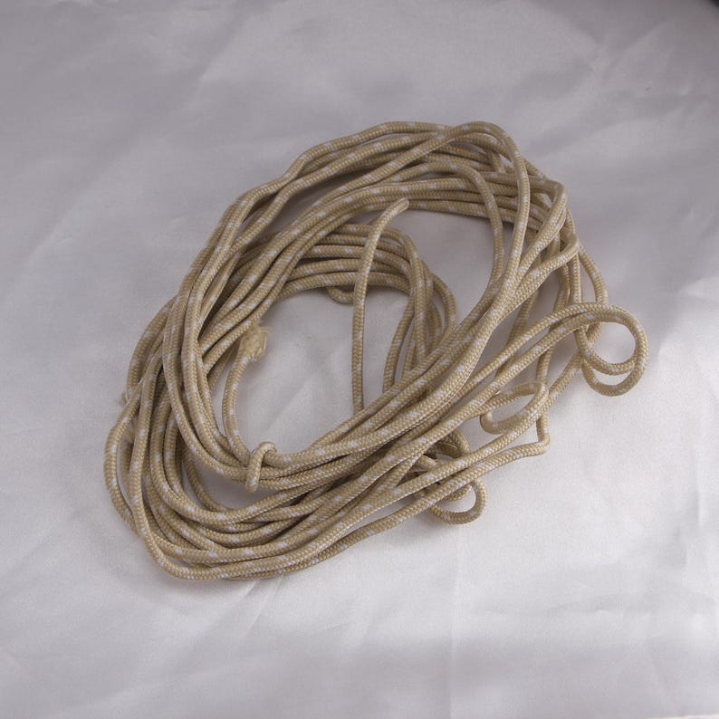 May include: A coiled rope with a tan and white speckled pattern. The rope is tightly wound, with visible strands and a knot. The neutral color palette suggests versatility for various uses, from crafting to outdoor activities.