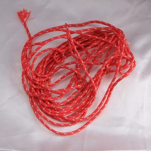 May include: A tangled coil of bright red rope with a white dotted pattern. The rope is tightly wound, with a frayed end extending from the top. The rope is likely used for crafting, climbing, or general utility purposes.