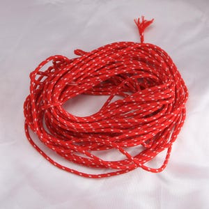 May include: Coiled red rope with a white dotted pattern. The rope is tightly wound, with a frayed end visible. The background is a plain white surface. This rope could be used for various crafting or outdoor projects.