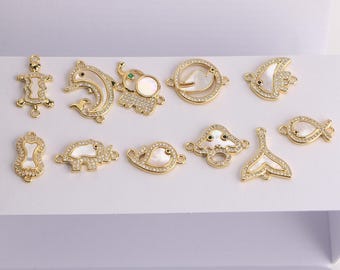 May include: A collection of gold-colored charms with various designs, including a turtle, dolphin, elephant, and fish. Each charm is embellished with clear crystals and a white shell inlay, creating a sparkling effect. The charms are likely for jewelry making.
