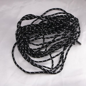 May include: A coiled length of black and white patterned rope. The rope is black with a repeating pattern of small white dots. The rope is tightly wound, creating a circular shape. The background is a plain white surface.