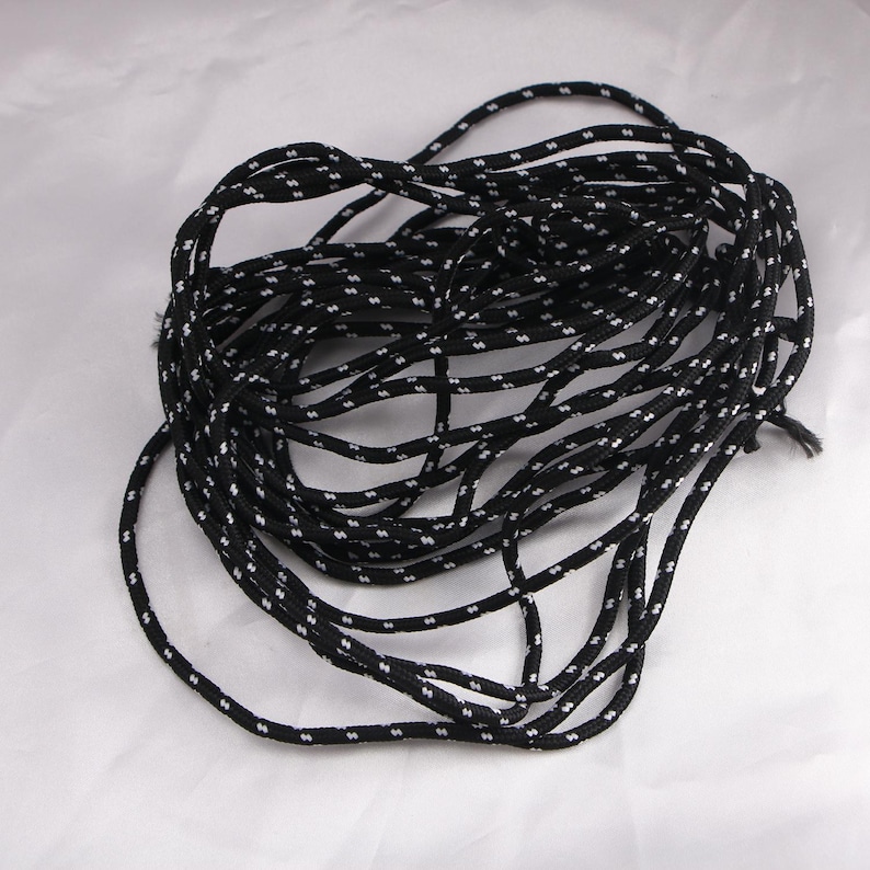 May include: A coiled length of black and white patterned rope. The rope is black with a repeating pattern of small white dots. The rope is tightly wound, creating a circular shape. The background is a plain white surface.