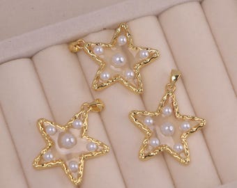Può includere: Tre ciondoli a forma di stella color oro con un centro trasparente e piccoli accenti di perle bianche. I ciondoli hanno un bordo strutturato e ondulato e un piccolo anello nella parte superiore per una catena. I ciondoli sono esposti su una superficie beige chiaro.
