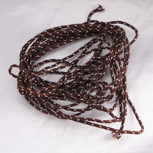 May include: Coiled brown and white patterned rope. The rope is tightly wound, with a repeating pattern of small white dots against a brown background. The rope is likely used for crafting or general use.