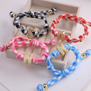 Peut inclure: Quatre bracelets colorés avec des breloques initiales dorées. Les bracelets présentent des motifs noirs et blancs, rouges et blancs, roses et blancs et bleus et blancs. Chaque bracelet a une perle dorée à chaque extrémité.