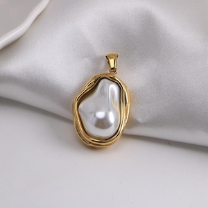 Op de afbeelding: Gouden hanger met een grote, onregelmatig gevormde witte parel. De hanger heeft een getextureerde gouden rand en een kleine lus voor een ketting. De parel heeft een glanzend, reflecterend oppervlak.