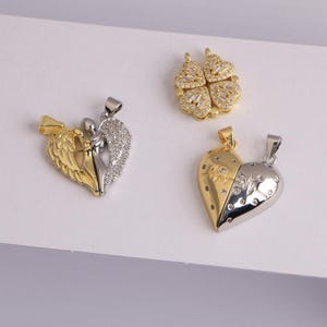 May include: Three gold and silver pendants are displayed against a white background. One pendant is a split heart design, another is a four-leaf clover, and the third is a heart with angel wings. Each pendant has a small loop for a chain.