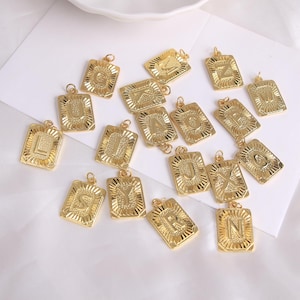 Op de afbeelding: Goudkleurige rechthoekige hangers, elk met een letter van het alfabet. De hangers hebben een getextureerde rand en een kleine lus om te bevestigen. De letters zijn in een vetgedrukte lettertype met schreef.