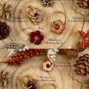 May include: A collection of flower-shaped earrings in various colors, including gold, glittery bronze, burgundy, and leopard print. Each earring has a gold hoop. The text "Mid Suzie" and "Mini Suzie" are visible.