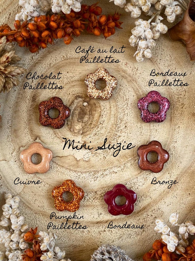 May include: A collection of flower-shaped embellishments in various colors, including copper, bronze, and burgundy, with glitter accents. The text "Mini Suzie" is handwritten in the center, with color names like "Pumpkin Paillettes" and "Bordeaux" labeling each piece.