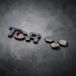 Puede incluir: Un conjunto de emblemas negros brillantes con las letras TCR en una fuente sans-serif audaz, acompañadas de tres pequeñas formas hexagonales negras. Cada pieza tiene un contorno rojo brillante a lo largo del borde inferior.