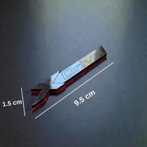 Peut inclure: Un emblème de voiture argenté avec le mot "Drive" et un éclairage d'accentuation rouge. L'emblème mesure 9,5 cm de long et 1,5 cm de large. L'emblème a un design en forme de clé.