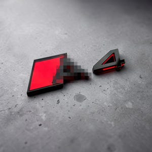 Op de afbeelding: Een zwart en rood embleem met een rechthoekige vorm en een gepixeld overgangseffect dat leidt naar een apart zwart en rood cijfer vier. Het ontwerp bevat scherpe geometrische lijnen en een hoog contrast in kleur met een matte afwerking.