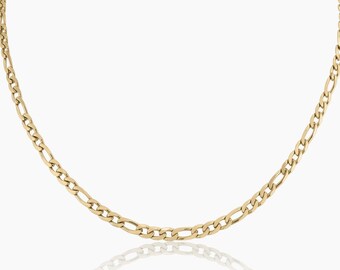 May include: A gold-colored Figaro chain necklace. The necklace features a pattern of alternating elongated and round links. The chain is displayed on a white background, with a slight reflection visible below.