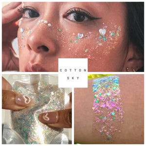 Puede incluir: Primer plano de un rostro adornado con purpurina iridiscente y adornos en forma de corazón. La imagen también muestra una bolsa de purpurina y una muestra en la piel, todo con un efecto brillante y multicolor. El texto "COTTON SKY" está en un cuadrado blanco.