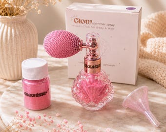 May include: A pink shimmer spray bottle with a bulb atomizer, a small jar of pink glitter labeled GLOWSSIS, and a small pink funnel. The spray bottle is in front of a white box labeled Hello Glow shimmer spray for Body & Hair.