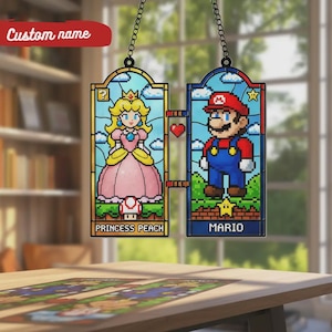 Puede incluir: Adornos de ventana de vidrieras con la Princesa Peach y Mario del videojuego Super Mario Bros. La Princesa lleva un vestido rosa y Mario un mono azul. Se muestran los textos "Princess Peach" y "Mario".