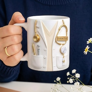 Könnte beinhalten: Weiße Keramiktasse mit einem Design eines Arztkittels, einschließlich goldfarbenem Stethoskop, Stift und Spritze. Die Tasse hat einen Griff und ein Taschen-Design. Der Text "Custom text" befindet sich auf der Tasse.