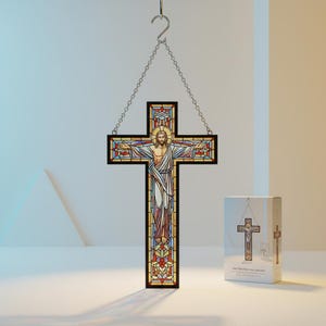 Puede incluir: Cruz de vidriera que representa a Jesucristo con los brazos extendidos, suspendida por una cadena. El diseño incorpora colores rojo, azul y amarillo. Una caja con una imagen similar está al lado de la cruz. Objeto religioso.