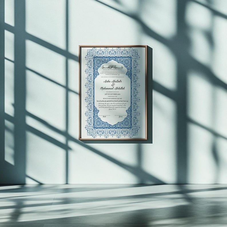 May include: A framed certificate with ornate blue and white designs. The certificate features Arabic script and English text, including names and a date. The frame is a light brown color, and the certificate is hanging on a white wall.
