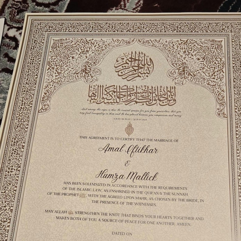 May include: A formal marriage certificate with ornate gold and brown decorative borders. The document features Arabic calligraphy and English text, including the names Amal Iftikhar and Humza Mallick. The certificate is a testament to a marriage solemnized under Islamic law.