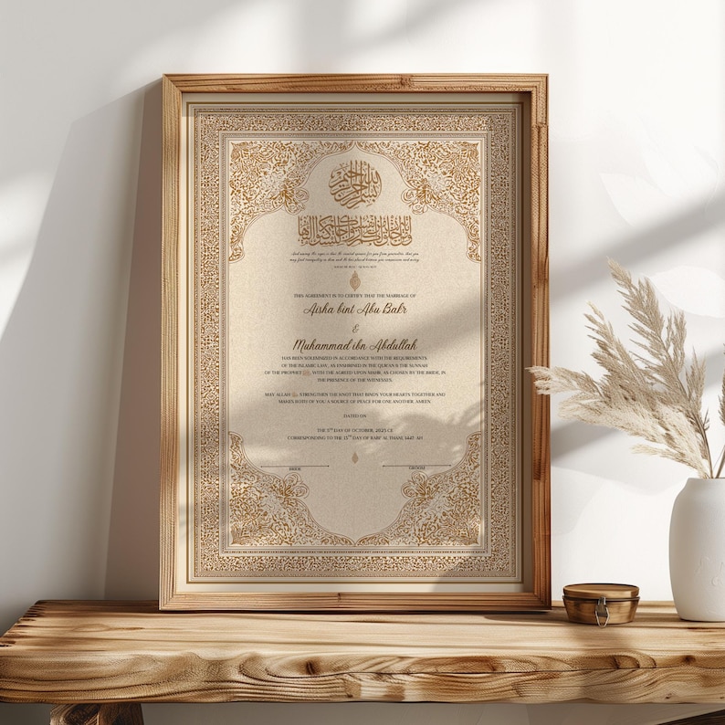 May include: Framed marriage certificate with ornate gold detailing and Arabic calligraphy. The document features the names Aisha bint Abu Bakr and Muhammad ibn Abdullah. The frame is a light brown color and sits on a wooden surface.