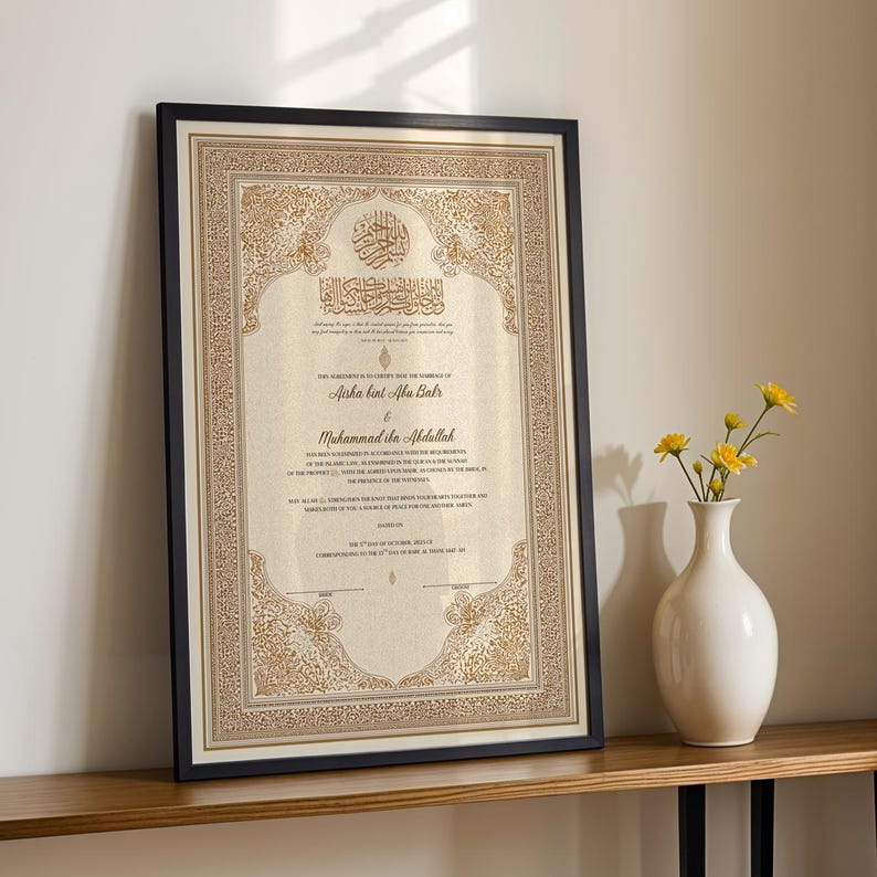 May include: Framed wedding certificate with ornate gold detailing and Arabic calligraphy. The certificate is in a black frame and rests on a wooden surface. A white vase with yellow flowers is to the right.