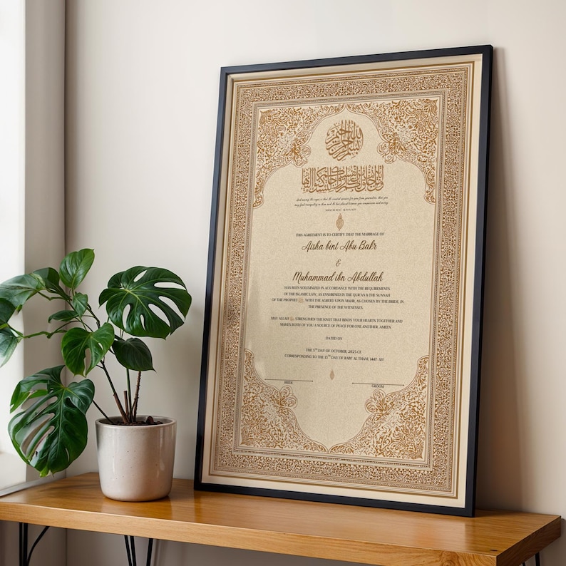 May include: Framed certificate with ornate gold and beige detailing, featuring Arabic calligraphy and English text. The black frame surrounds the document, which is leaning against a wall. A potted plant sits on a wooden surface in the foreground.