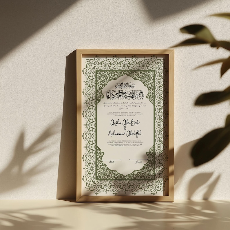 May include: A framed print featuring Arabic calligraphy and English text. The print has a light green and cream color scheme with decorative borders. The names "Aisha Abu Bakr" and "Muhammad Abdullah" are written in elegant script.