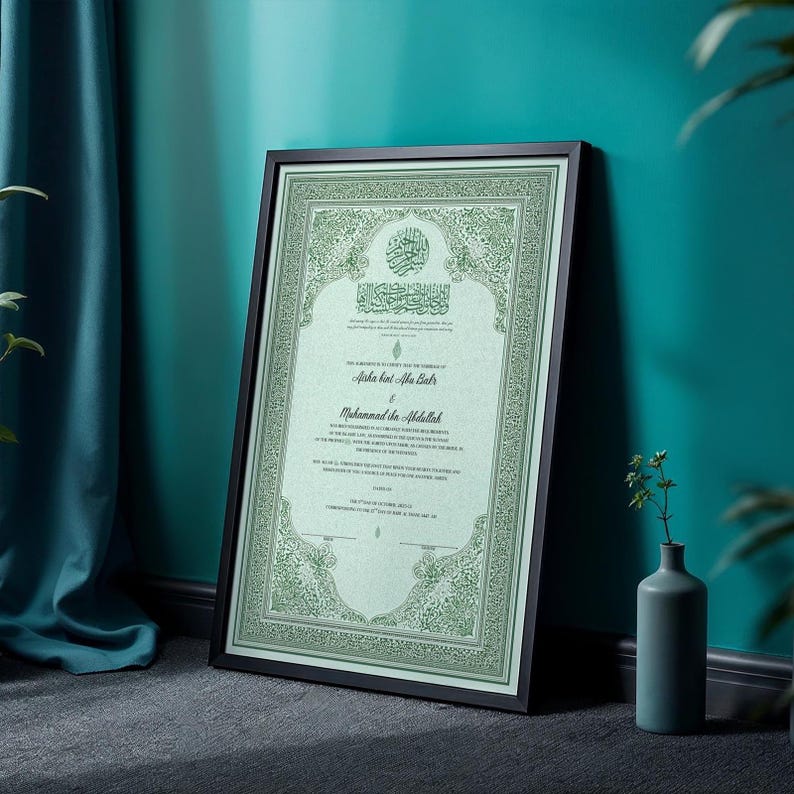 May include: Framed Islamic marriage certificate with ornate green border and text. The certificate is in a black frame, leaning against a teal wall. A small vase with greenery sits nearby. The certificate features Arabic calligraphy and English text.