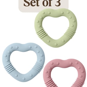 May include: Set of 3 heart-shaped baby teethers in pastel colors. The teethers are green, blue, and pink, with textured surfaces and small circular bumps. Each teether has a ribbed section and the text "Set of 3" is in the background.