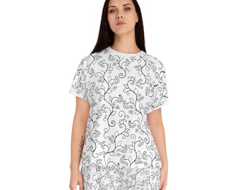 May include: White pajama set with a black floral design. The set comprises a short-sleeved top and matching shorts. The pattern features swirling vines, leaves, and berry-like clusters, offering a delicate, nature-inspired aesthetic.
