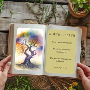 Może przedstawiać: Otwarta książka z akwarelową ilustracją drzewa z kolorowymi liśćmi na lewej stronie oraz tekstem NORTH - EARTH, I am rooted in myself. I do not seek stability. I embody it. The ground beneath me holds me. WhisperLight & Co.