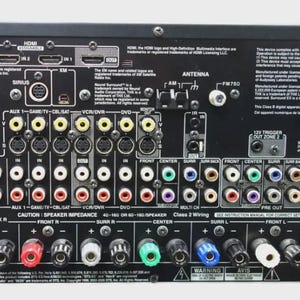 May include: The black rear panel of an Onkyo TX-SR805 AV receiver featuring numerous input and output ports, including HDMI, component video, digital audio, and speaker terminals, with printed technical specifications and regulatory markings.