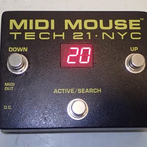 Puede incluir: Un pedal MIDI Mouse Tech 21 NYC negro con texto amarillo, que presenta tres interruptores de pie de metal plateado etiquetados como DOWN, UP y ACTIVE/SEARCH. Una pantalla digital roja muestra el número 20. La unidad incluye etiquetas para MIDI OUT y D.C.