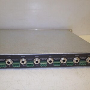 May include: A silver-colored audio mixer with multiple input and output jacks. The front panel features numerous ports labeled "Insert" and "Mic/Phaline Switch," along with green connectors. The device is designed for professional audio applications.