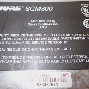 May include: A black label with white text for a Shure SCM800 audio product. The label includes safety warnings, manufacturer information, and UL and SP certifications. A sticker with a barcode and the product model is also present.
