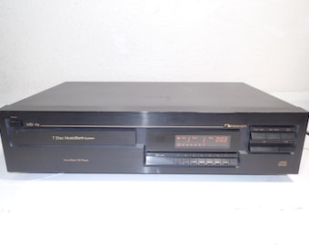May include: Black Nakamichi MB-4s 7 Disc MusicBank System CD player. The unit has a digital display showing track and time information. The front panel has several buttons and a CD tray.