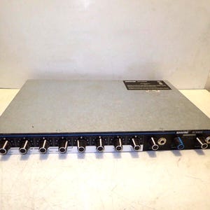 May include: A silver and black Shure SC3400 audio mixer with multiple knobs and input jacks. The mixer has a black front panel with blue accents and white text. The device is designed for professional audio applications.