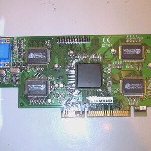 Pode incluir: Uma placa de circuito verde com vários componentes eletrônicos, incluindo chips e conectores. Possui um conector VGA azul e um suporte de metal. A placa tem o texto "DIAMOND" e o ano "1997" impressos.