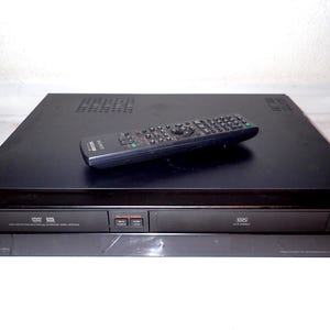 May include: A black Sony DVD/VHS player with a remote control. The player has a sleek design with a DVD tray and VHS slot. The remote is black with multiple buttons. The player is on a white surface.
